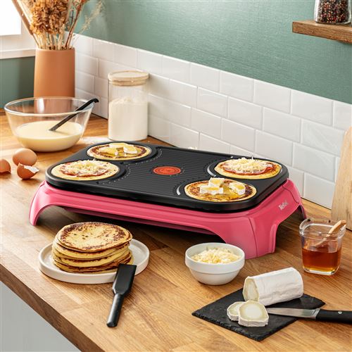 Tefal elektrische pannenkoekenmaker en grill met pannenkoeken, glazen kom met beslag, gesneden rolkaas, stapel pannenkoeken, bokaal jam, eieren, suiker en spatel in de keuken