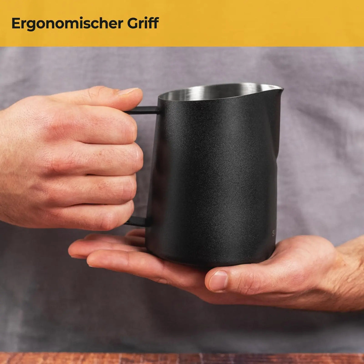 Zwarte Silberthal RVS melkkan voor latte art met ergonomisch handvat, vastgehouden met twee handen.