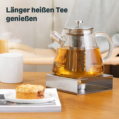 Silberthal glazen theepot op een theewarmer, met een gebakje op een wit bordje

